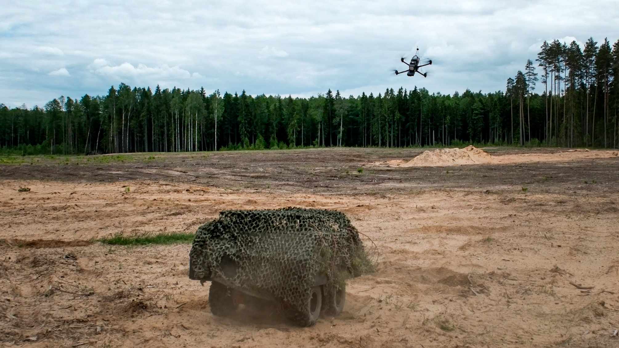 Flying drone targeting an unmanned ground vehicle (UGV) during the training Military training ground. A flying drone is monitoring an unmanned ground vehicle.